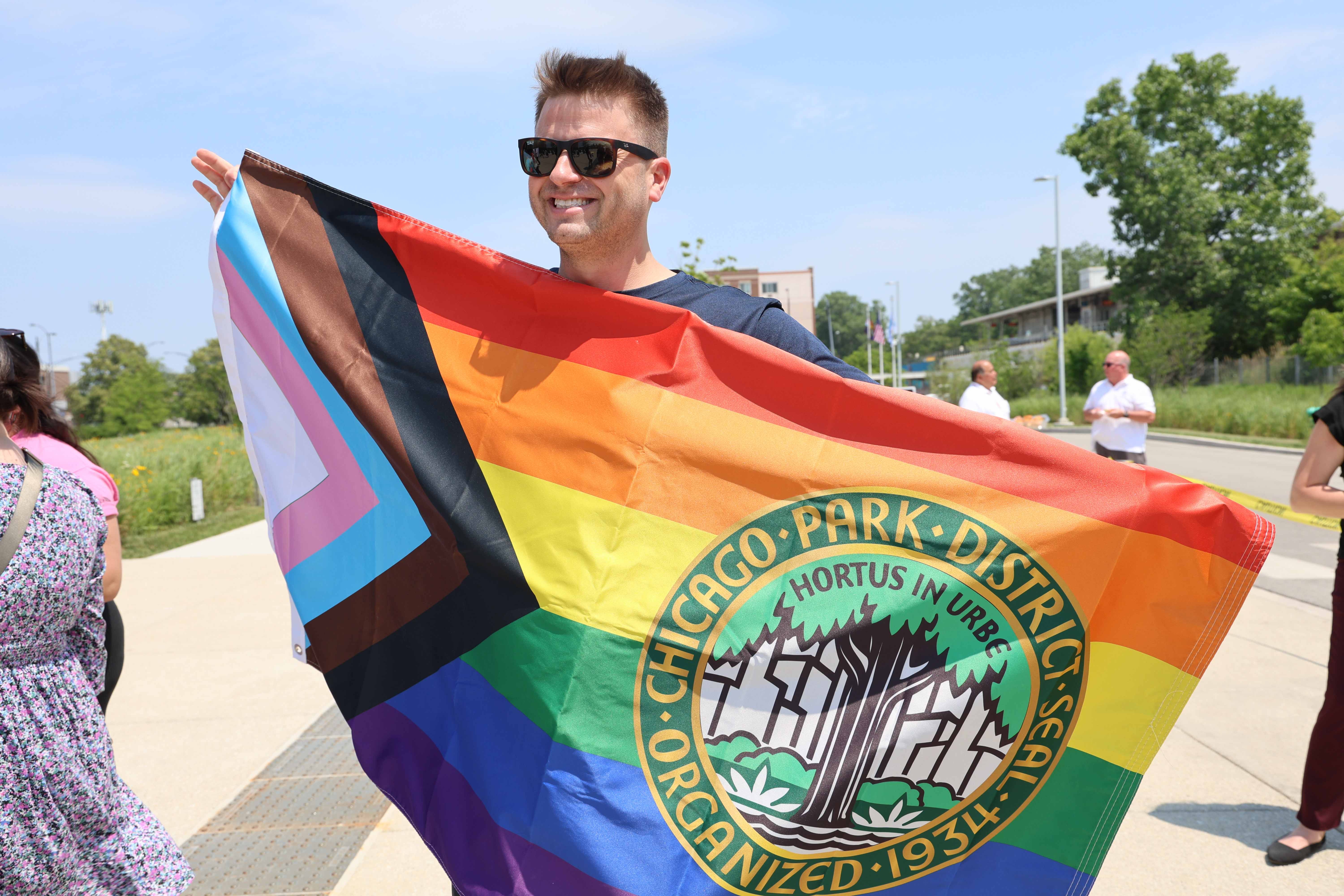 Smiling person holding a Progress Pride flag with the Chicago Park District logo.