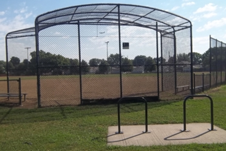 Empty baseball field behind backstop. Bike rack in foreground.