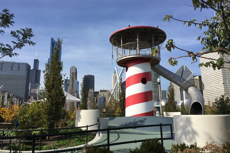 Red and white lighthouse-shaped playground slide with metal tube slide and Chicago skyline in background.