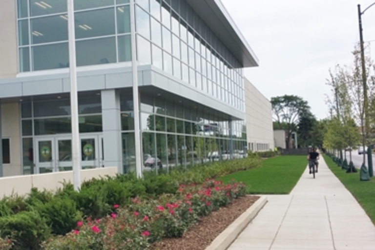 Modern building with glass facade, landscaped walkway, and cyclist.
