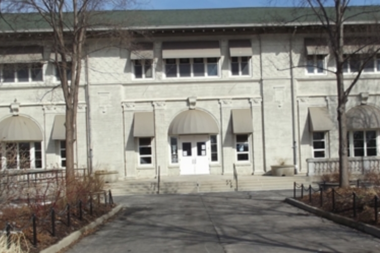 Exterior of a light gray stucco community building with a double door entrance.