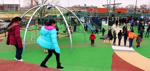 Children play on a colorful playground. Climbing dome, slides, and people in background.
