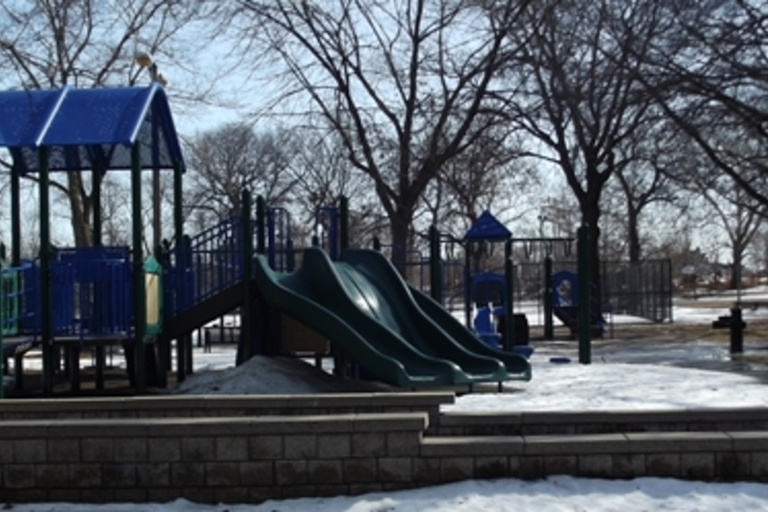 Playground with slides and climbing structures in a park dusted with snow.