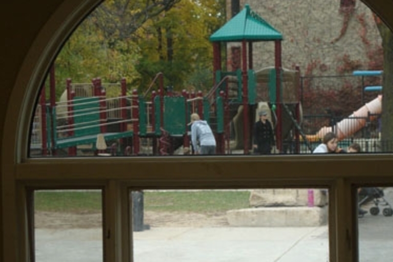 Children playing on a playground viewed through arched and rectangular windows.