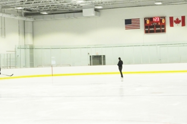 Vast indoor ice rink with a hockey player and a figure skater.