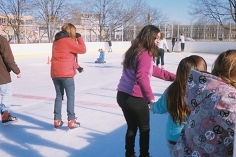 People ice skating at an outdoor rink on a sunny day.