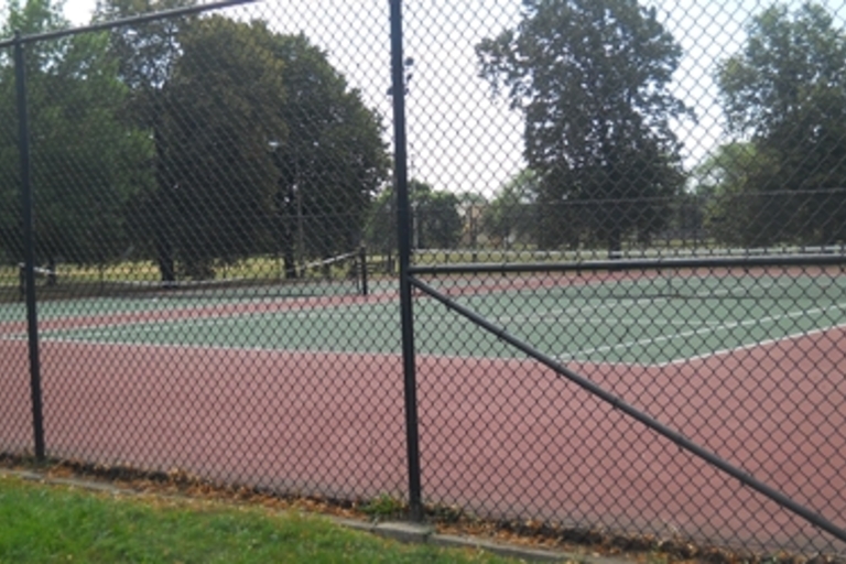 Empty tennis courts seen through chain link fence.