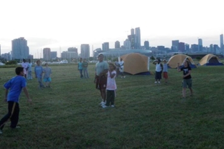 People playing in a field with tents and a city skyline in the background.
