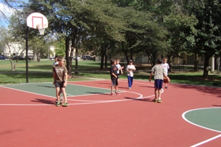 Children playing basketball on a red and green court in a park.