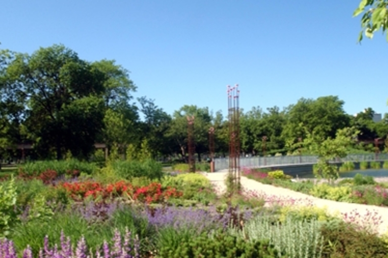 Vibrant flower garden with a path leading to a pond and modern sculpture.