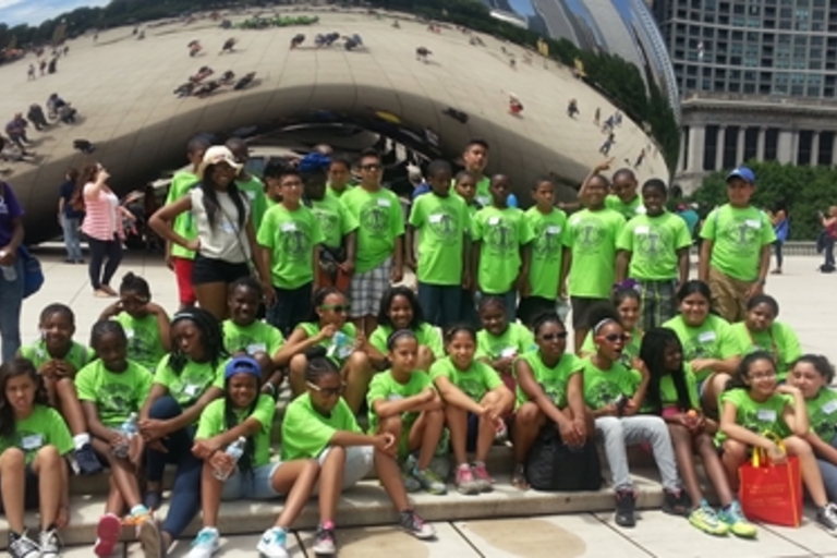 Group of students in matching green t-shirts pose in front of Chicago's Cloud Gate sculpture.
