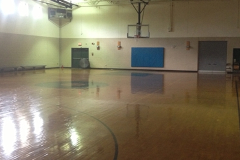 Empty gymnasium with polished wooden floor and basketball hoop.