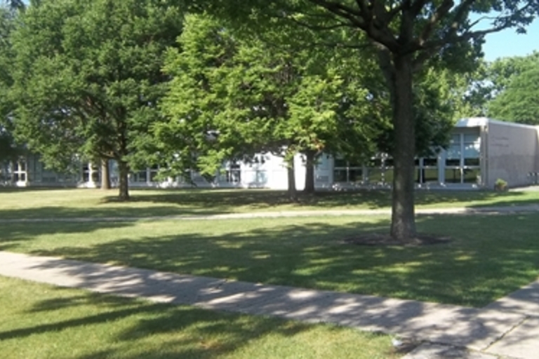 Shady green lawn and trees in front of a single-story school building.