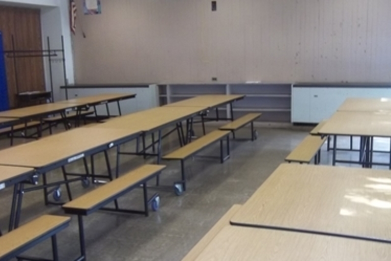 Empty school cafeteria with long tables and attached benches.