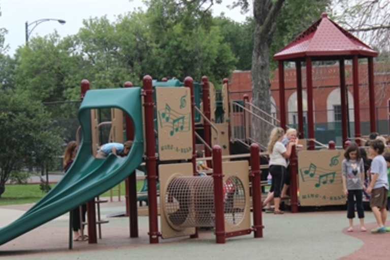Children play on a colorful playground structure with a slide and climbing features.
