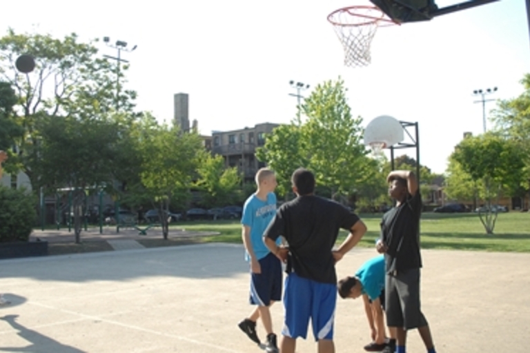 Young men play basketball on an outdoor court.
