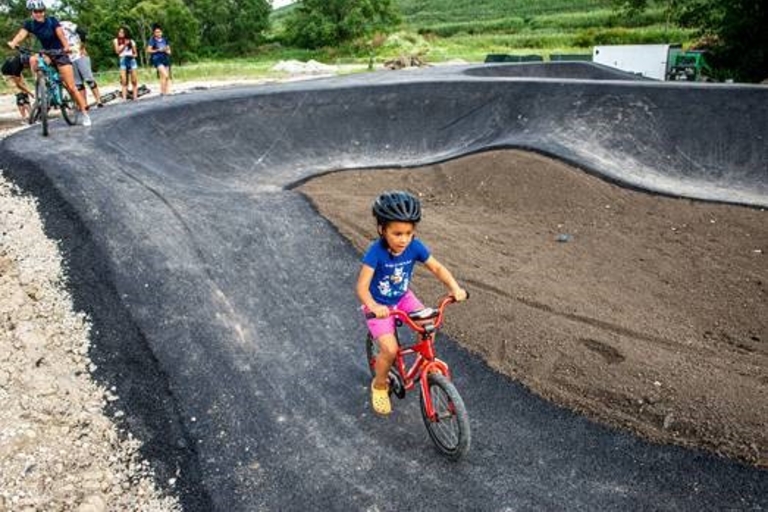 Child rides bike on paved pump track.