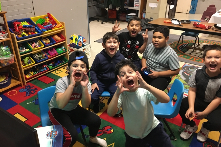 Five children excitedly yell and gesture in a playroom.