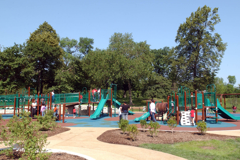 Children and adults play on a playground with slides and climbing structures on a sunny day.