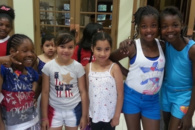 Group of girls smiling for a photo. Several wear red, white, and blue.