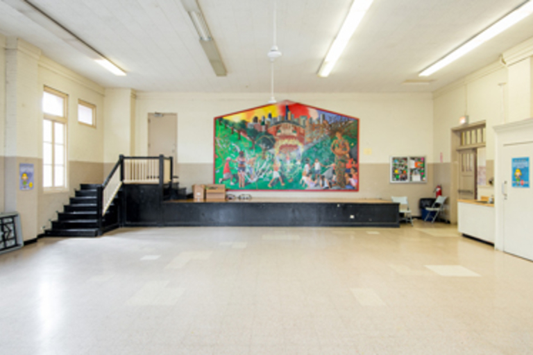 Large room with a colorful mural, small stage, and speckled tile floor.