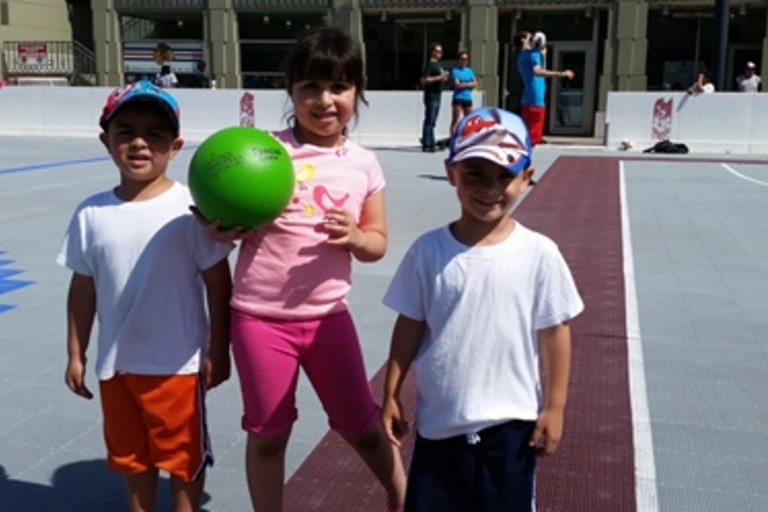 Three children on a playground, one holding a green ball.
