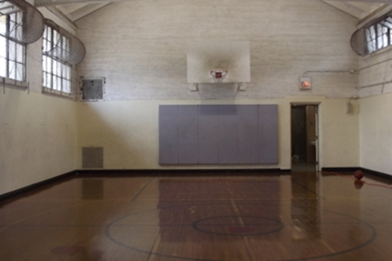 Empty indoor basketball court; children sit on sidelines.