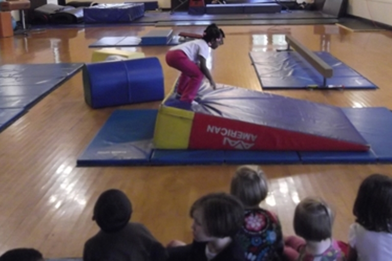 Gymnastics instructor demonstrates a maneuver on a wedge mat to a group of children.
