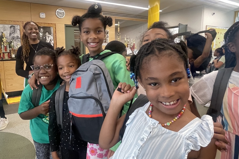 Smiling students with backpacks gather in a school hallway.
