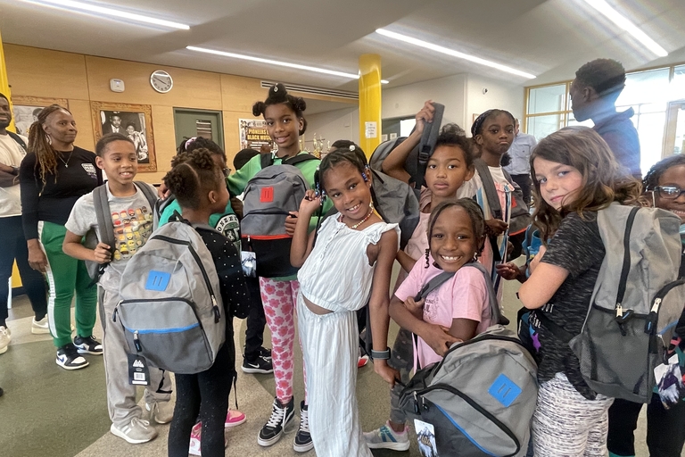 Group of children with backpacks smiling in school hallway.