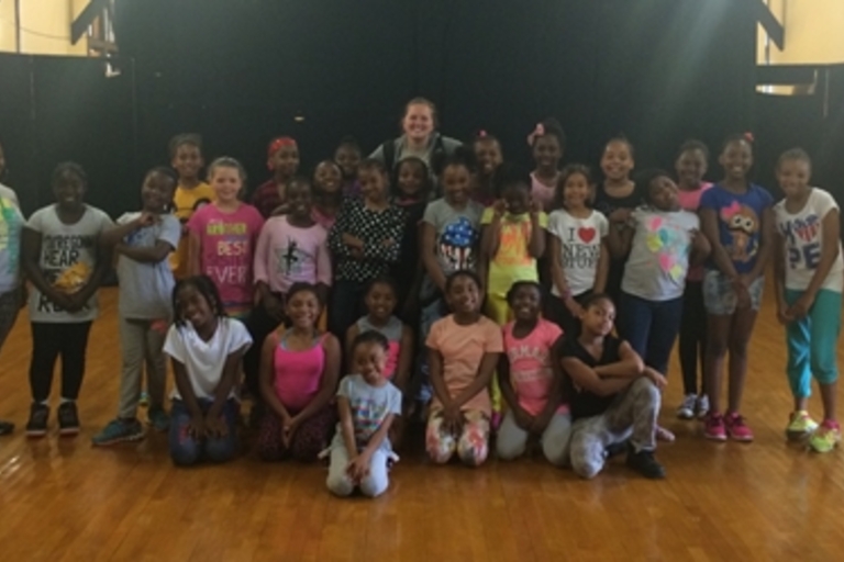 Large group of girls and their instructor pose for photo in dance studio.