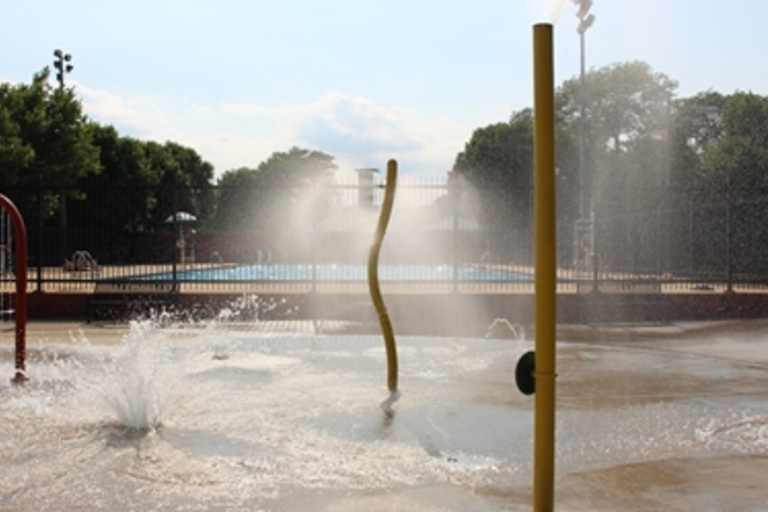 Splash pad with water jets in front of a swimming pool.
