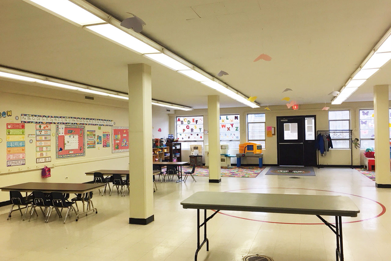 Bright preschool classroom with small tables and chairs, learning materials, and paper butterflies hanging from the ceiling.