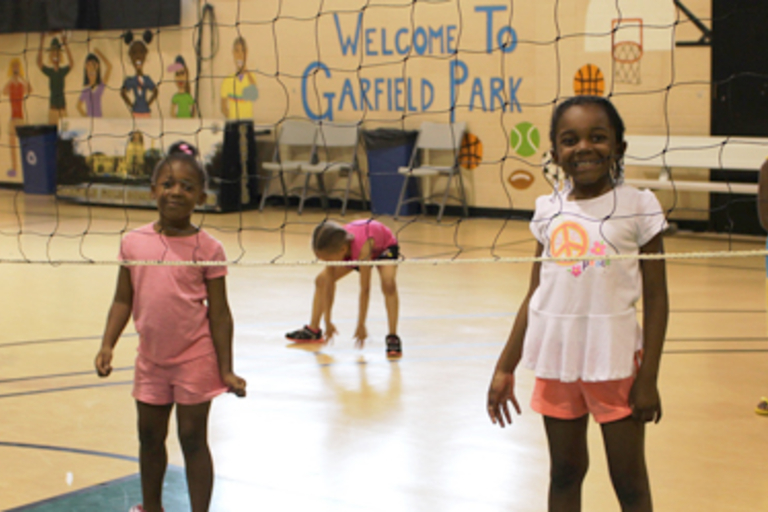Smiling girls in a gymnasium behind a volleyball net.