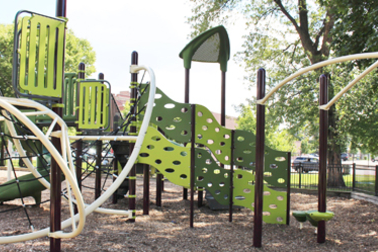 Green and brown playground structure with climbing wall and rope ladder.