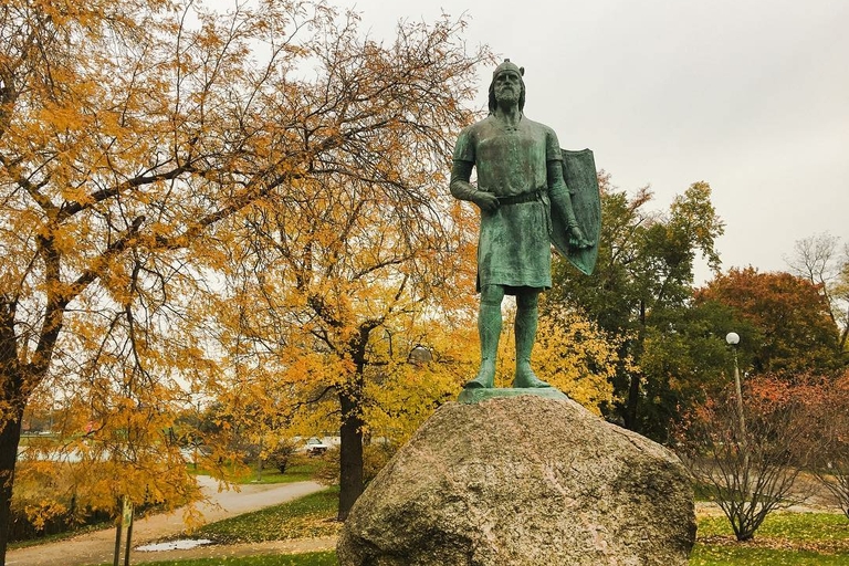 Bronze statue of a Viking with a shield, standing on a rock in a park during autumn.