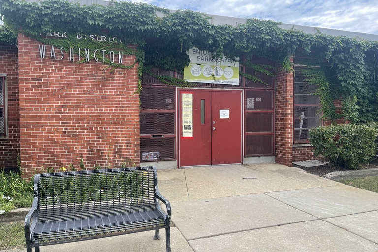 Washington Park District building exterior with red doors and vine-covered brick. A black metal bench sits in front.