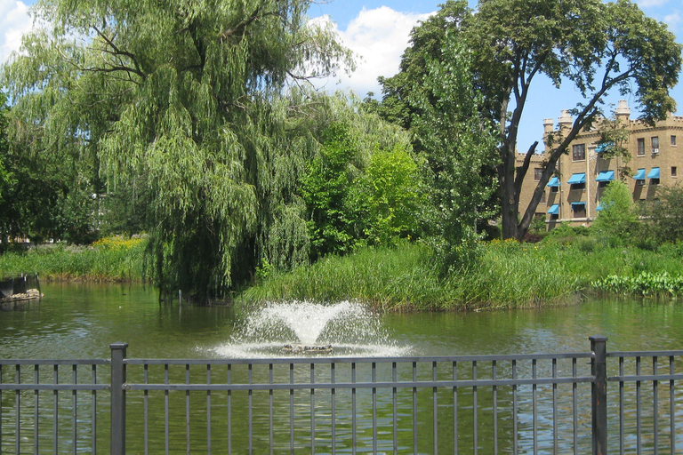 Small pond with a fountain, surrounded by greenery and a brick apartment building.