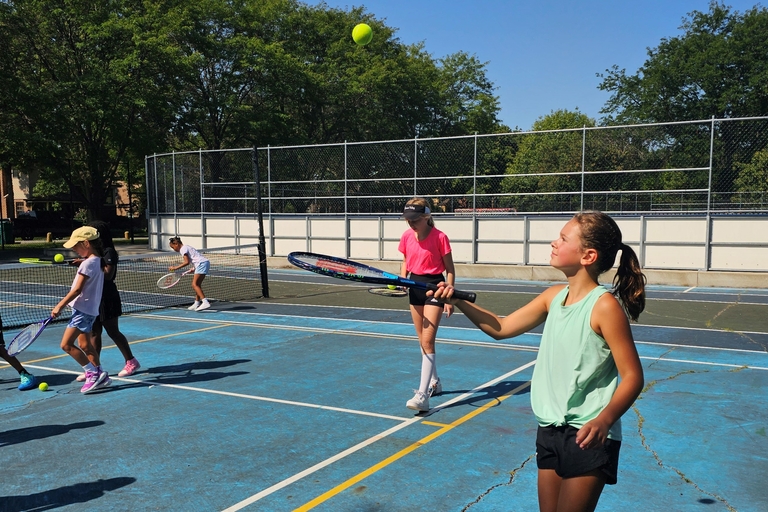 Children playing tennis on a blue court.