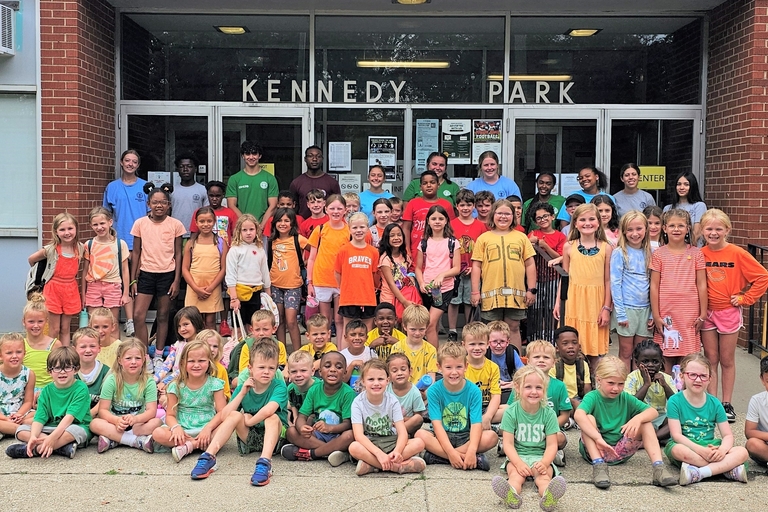 Large group of children and teenagers pose outside Kennedy Park building.
