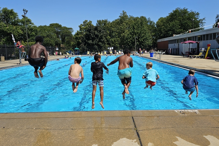 Six children mid-air jumping into a bright blue swimming pool on a sunny day.