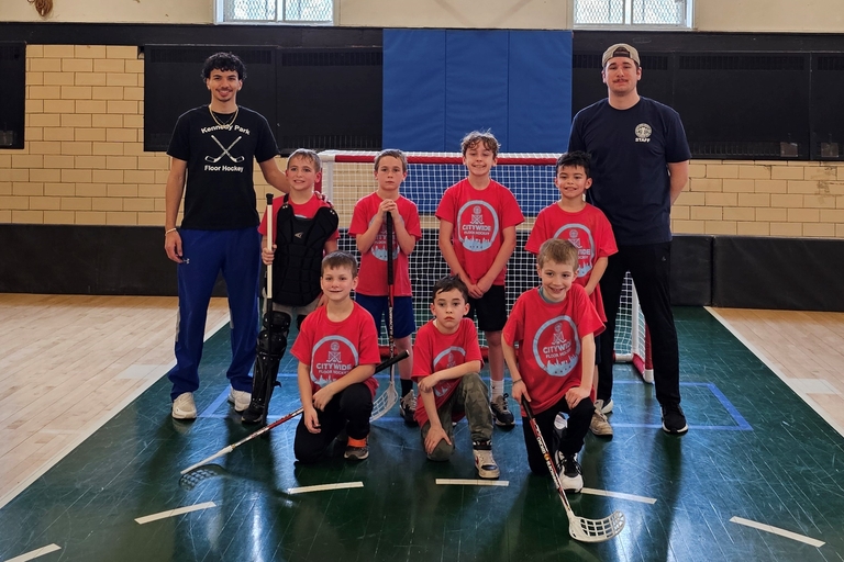 Youth floor hockey team and coaches pose for a photo on the court.