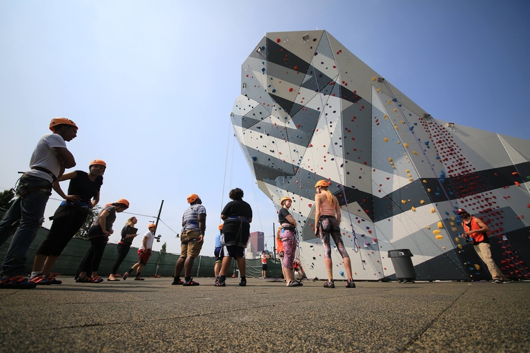 Climbers prepare at the base of a large outdoor climbing wall.
