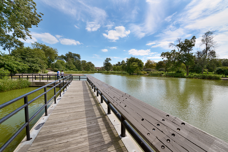 Wooden walkway over a lagoon in a park. Two people stand at the far end.
