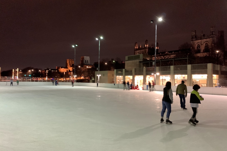 People ice skating at night on an outdoor rink. A large church is visible in the background.
