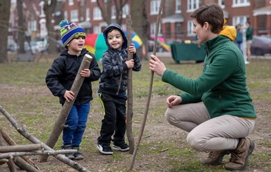 Two children and a park worker play with sticks in a park.