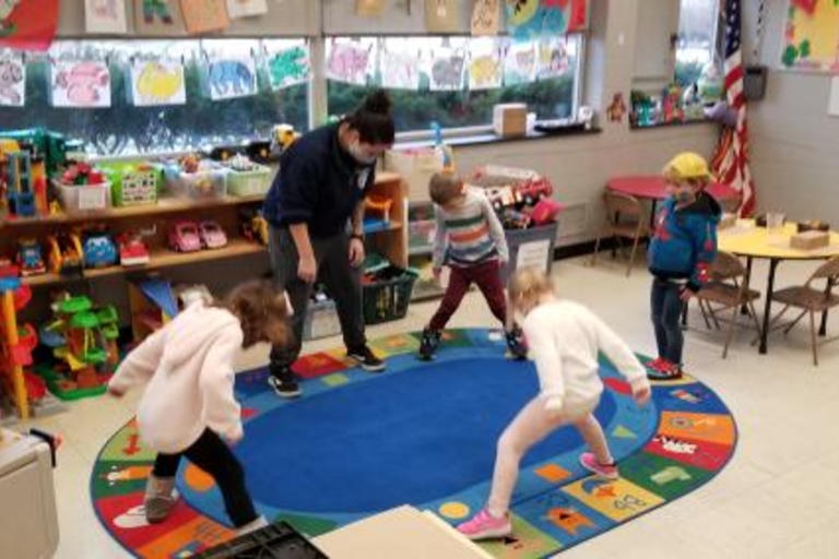 Preschoolers and teacher doing stretches on blue classroom rug.