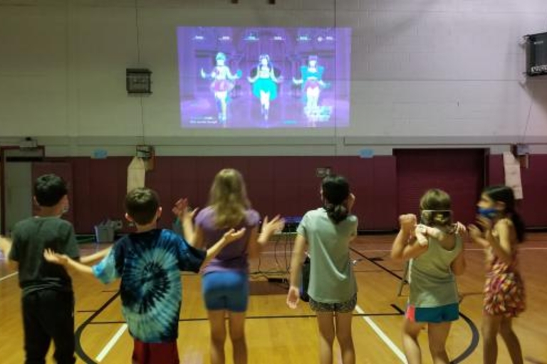 Children dancing to projected video game in gym.