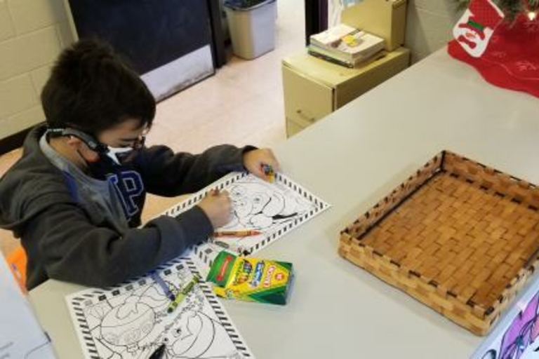 Boy wearing a mask coloring Christmas pictures with crayons.