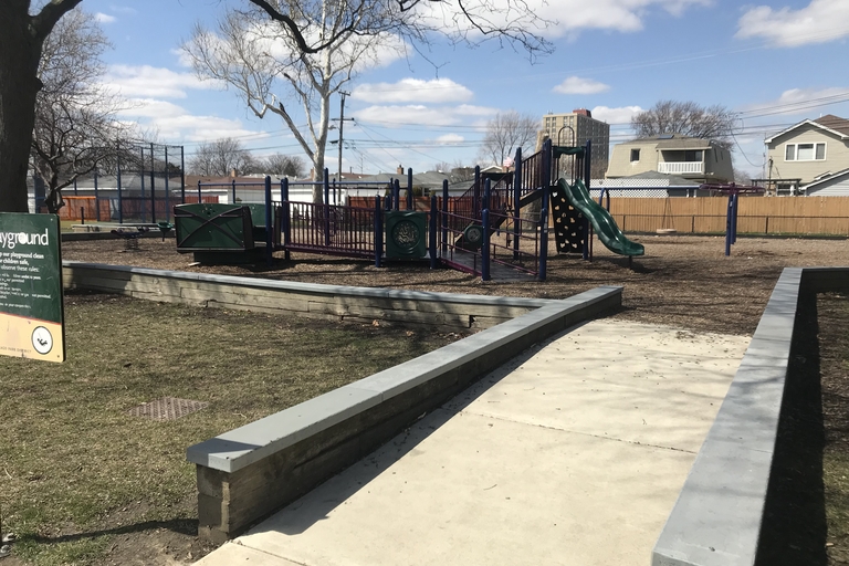 Playground with a green slide and climbing structures. Paved walkways surround the play area.